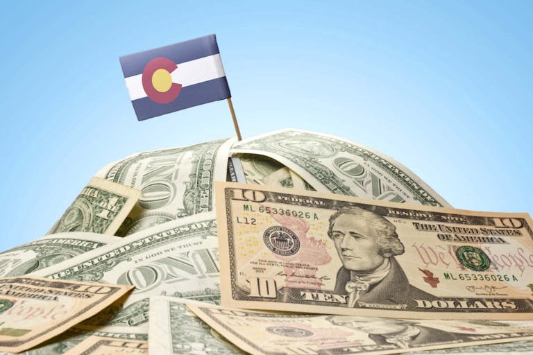 Photo: Getty Images The national flag of Colorado sticking in a pile of american dollars.(series)
