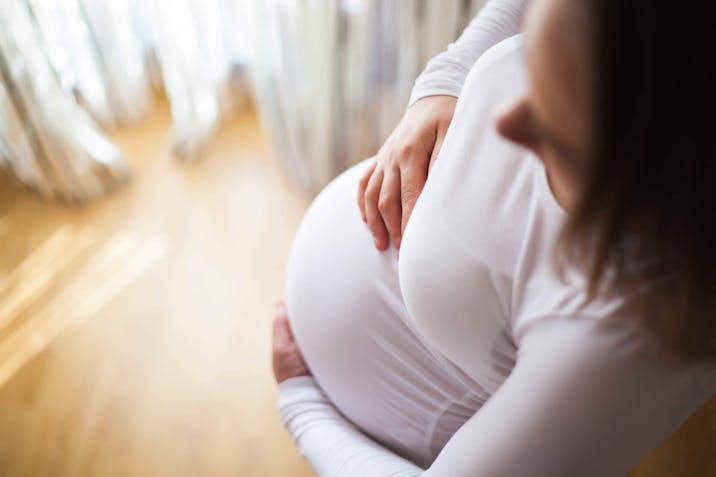 A pregnant woman holds her bump feeling positive