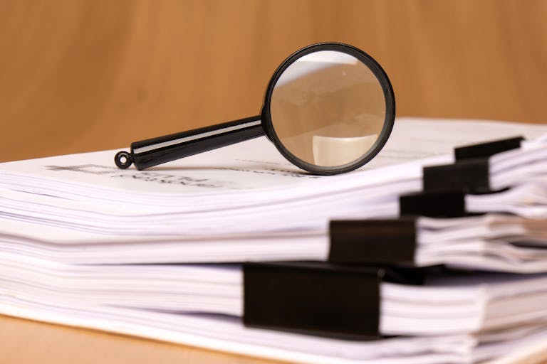 Photo: Getty Images A magnifying glass rests on scattered clipped papers, symbolizing diligent research and careful analysis