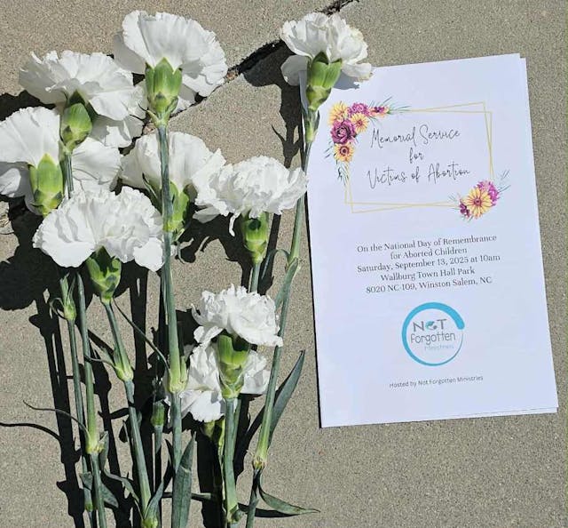Day of Remembrance in Winston-Salem, NC (Photo: Tori Shaw) white carnations sit on the concrete next to a white bulletin about the Day of Remembrance