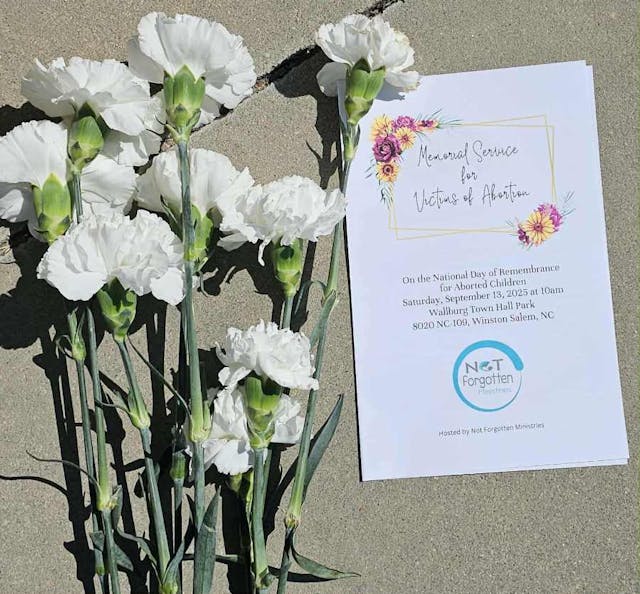 white carnations sit on the concrete next to a white bulletin about the Day of Remembrance