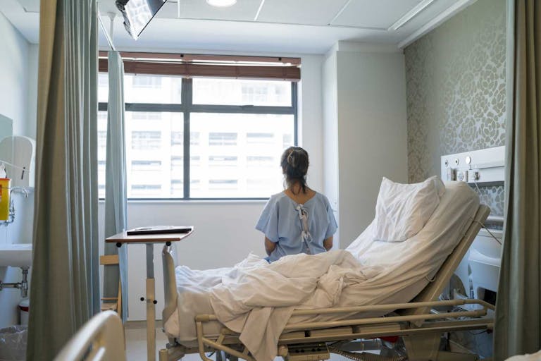 Photo: Stígur Már Karlsson /Heimsmynd via Getty Images Rear view of female patient sitting on bed wearing a hospital gown