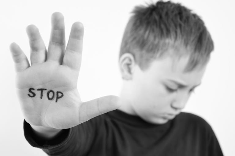 Photo: Getty Images Small abused boy holding his hand with the word ‘STOP’ written on it.