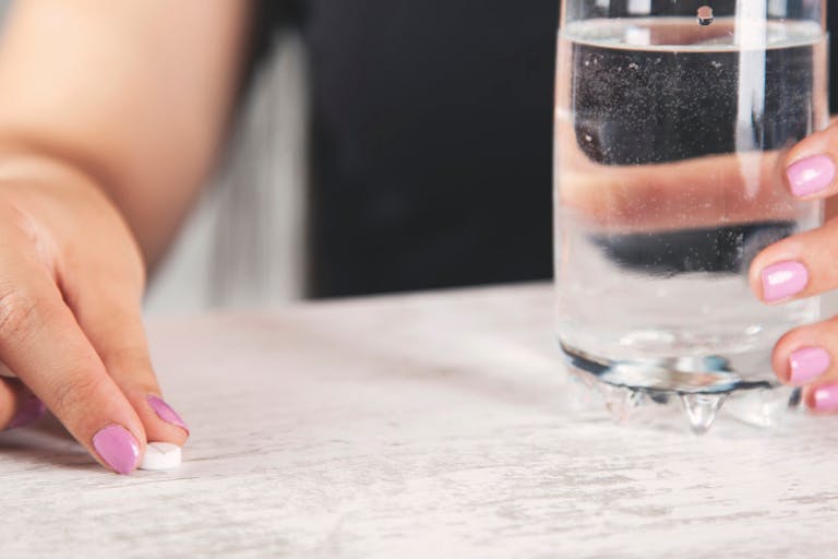 woman hand drug and water glass on desk