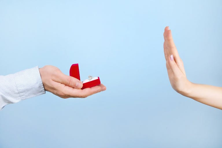 She said NO concept. Young girl rejects the marriage proposal. Woman refuses the engagement gold platinum diamond ring, man male & female hands close up, NO gesture. Blue background, copy text space.