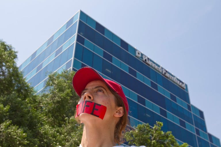 Photo: Nick de la Torre/Houston Chronicle via Getty Images A woman wearing a red hat and with red tape over her mouth with "LIFE" written on it stands in front of a Planned Parenthood facility in Houston, Texas.