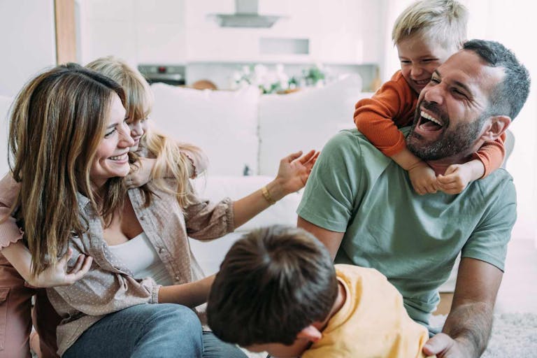 Shot of cheerful parents with their three kids playing on the floor in living room at home.
