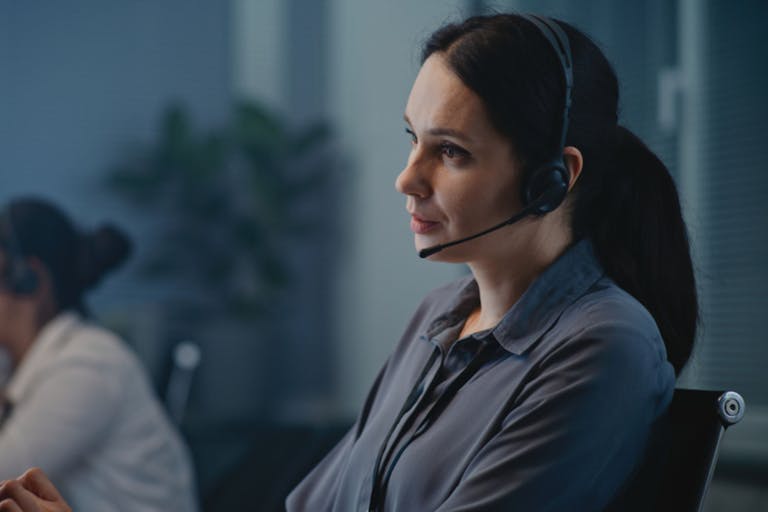 Photo: EvgeniyShkolenko/Getty Images Call center office of mental health helpline: Close up of Caucasian female crisis hotline worker talking on headset, consulting person online, providing psychological help. Emotional support concept.