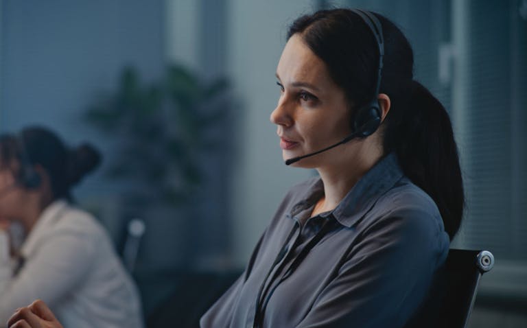 Call center office of mental health helpline: Close up of Caucasian female crisis hotline worker talking on headset, consulting person online, providing psychological help. Emotional support concept.