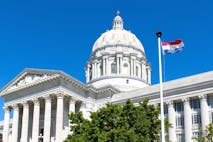Image shows the Missouri state flag flying in front of the Missouri state capitol building.
