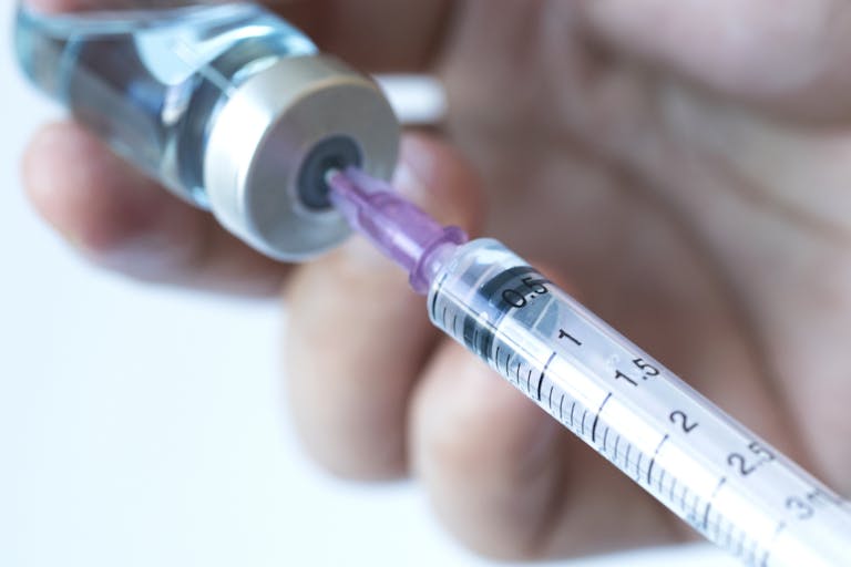 Photo: Ake Ngiamsanguan/Getty Images Doctor's hand holds a syringe and a blue vaccine bottle at the hospital. Health and medical concepts stock photo