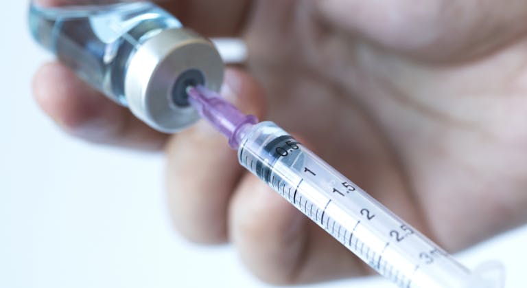 Doctor's hand holds a syringe and a blue vaccine bottle at the hospital. Health and medical concepts stock photo