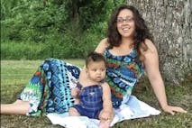Mother sits by a tree with her young son, who is dressed in bib overalls