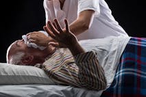 Nurse trying to suffocate her patient to death while he is sleeping on black background