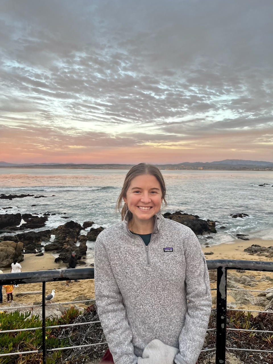Jane Allen smiles standing in front of a bay in 2023.
