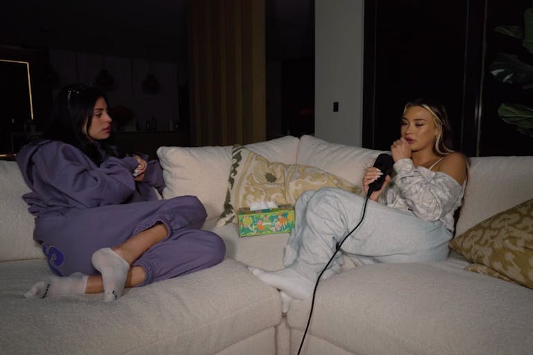 Screenshot from YouTube interview Image shows two women sitting on a couch in their pajamas with a box of tissues sitting between them.