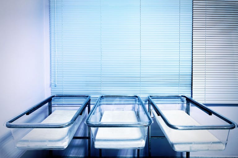 Photo: vasiliki/Getty Images Baby cribs at a maternity ward. Low birth rate and fertility concept.