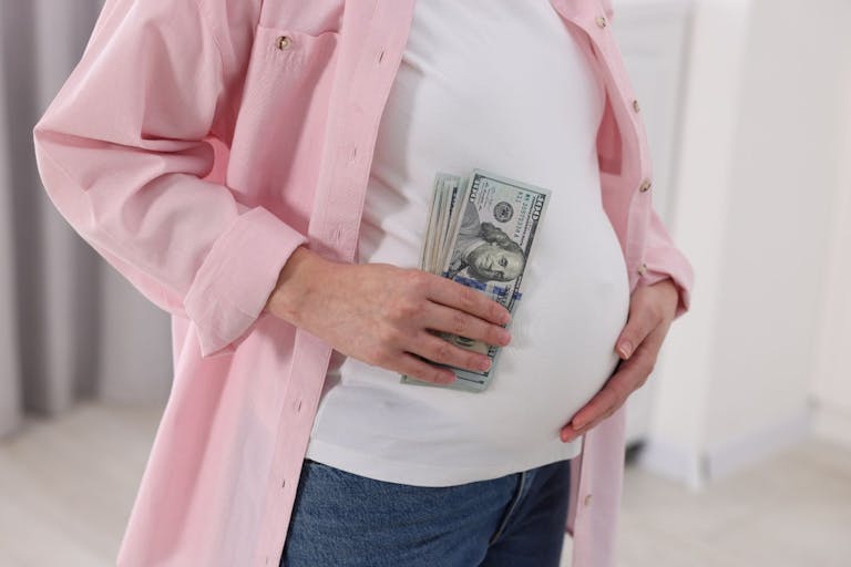 Photo: Liudmila Chernetska/Getty Images Surrogate mother. Pregnant woman with dollar banknotes indoors, closeup