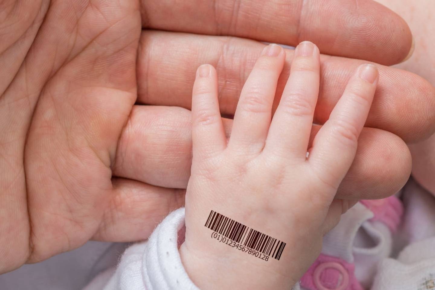 An adult holds a baby's hand that is stamped with a barcode.