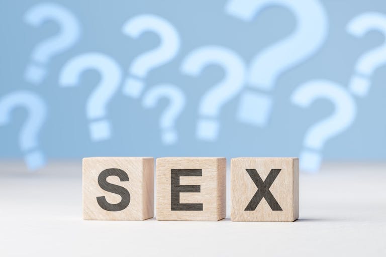 Sex question. Sexual Health, Sex education. Word sex is laid out with wooden cubes on background of many question marks.
