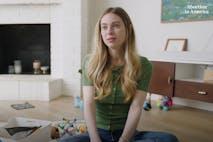 Screenshot: 'Abortion in America' (YouTube) Woman with long blonde hair and a green shirt sits on the floor in a living room surrounded by toys.