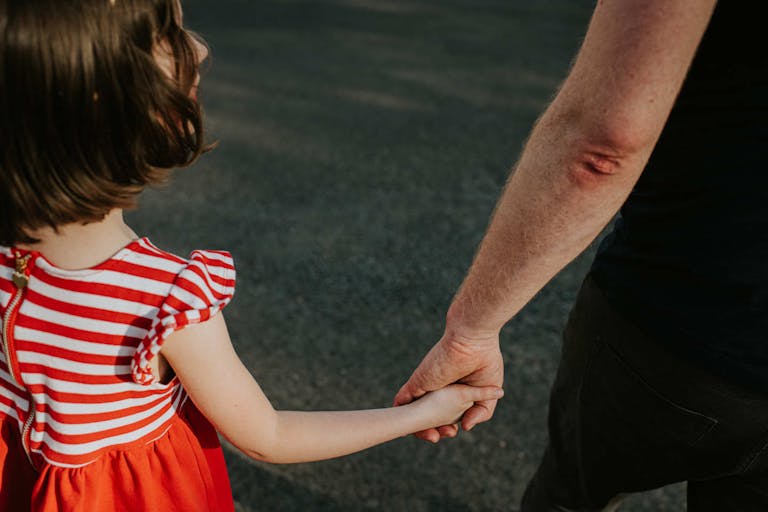 Photo: Catherine Falls Commercial/Getty Images A little girl walks along side an adult male. They hold hands as she glances up at him. Conceptual with space for copy.