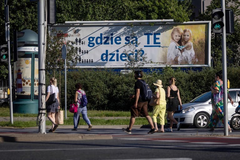 Photo by WOJTEK RADWANSKI/AFP via Getty Images Pedestrians cross a street near a billboard with a poster with the lettering reading 'Where are these children?' in Warsaw, on August 5, 2022. - The billboards, put up in recent weeks by a Catholic foundation, are hard to miss: large and plastered all over Poland, they show two little blonde girls in immaculate white posing in a wheat field -- along with the alarmist caption, "Where are these children?" Falling birth rate statistics displayed alongside in the form of a pictogram claim that the average Polish family had five children in the 1950s, down to three in the 80s and 1.5 today.
