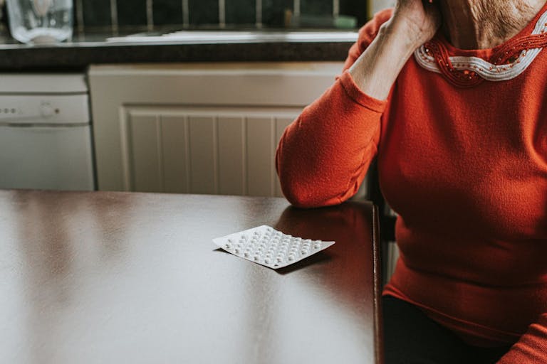 Getty Images Credit: Catherine Falls Commercial A blister pack of tablets sits on a wooden table. An elderly woman rests her chin on her hand and looks at the medication infront of her.