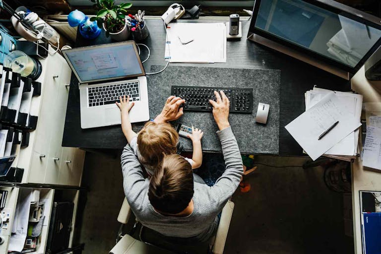 Photo: Franziska & Tom Werner/Getty Images An aerial view of a mother working on a laptop in her office at home with her young daughter sitting on her lap.