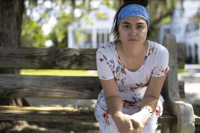 Rosalie Markezich sits on a bench wearing a blue headband and a white dress with organ and green leaves.