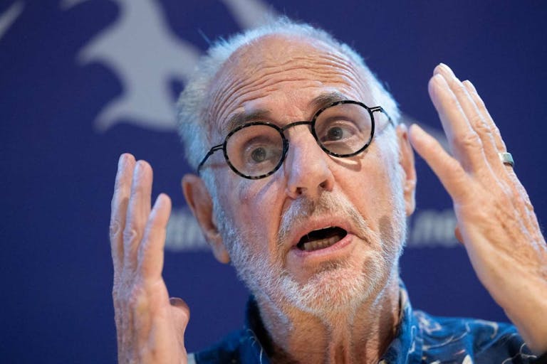 Australian euthanasia activist Philip Nitschke addresses a press conference of The Last Resort, a Swiss newest human rights, non-profit association focused on assisted suicide, to present the Sarco in Zurich on July 17, 2024. An assisted suicide capsule, which is causing a stir in Switzerland, could be used "very soon" for the first time, The Last Resort, the organization promoting it, estimated on July 17, 2024, without giving further details at this stage. The futuristic-looking device, called "Sarco" for sarcophagus, is designed to enable people to take their own lives by pressing a button inside the capsule, which is supposed to release nitrogen. (Photo by ARND WIEGMANN / AFP) (Photo by ARND WIEGMANN/AFP via Getty Images) Dr. Philip Nitschke sits with hands raised in a blue collared shirt in front of a blue background, as he speaks to the press about assisted suicide.