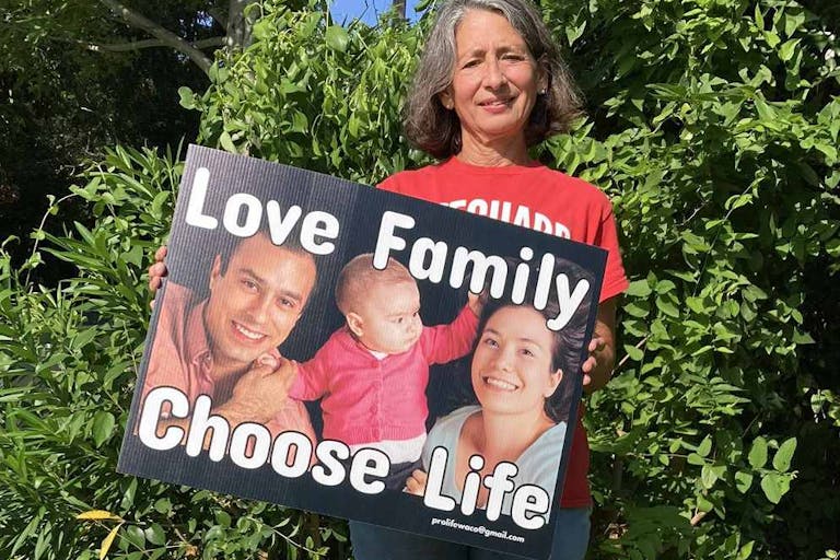 Photo: Pro-Life in the Public Square woman holds yard sign that says "Love Family, Choose Life"