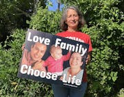 woman holds yard sign that says "Love Family, Choose Life"