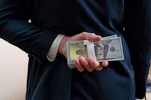 Photo: Kmatta/Getty Images Businessman holding money money us dollar behind his back, rear view.