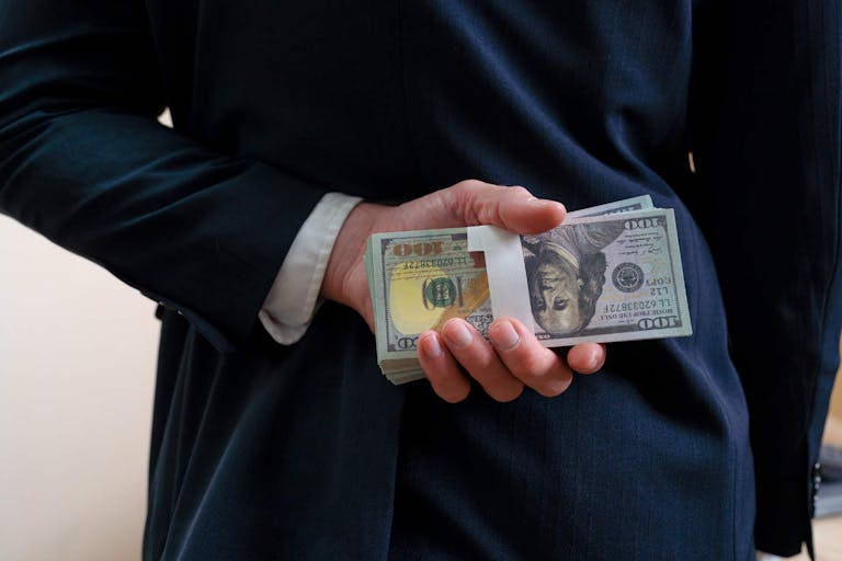 Photo: Kmatta/Getty Images Businessman holding money money us dollar behind his back, rear view.