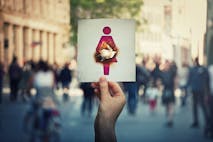 Miscarriage and fetus loss concept as hand holding a paper with woman icon symbol has broken abdomen as a burnt hole in stomach. Human spontaneous abortion message over a crowded street background.