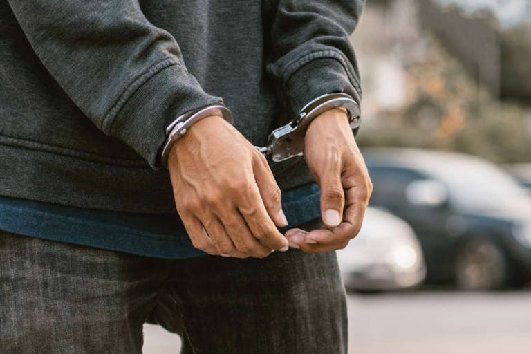 Under arrest, a man's hands with clenched fists are handcuffed behind him.