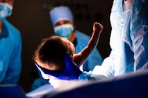 Baby delivered and raising arm and fist during C Section procedure in Hospital Operating Room - stock photo