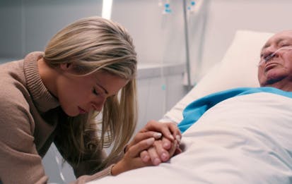 Healthcare, senior man and sad woman in hospital for support, love and praying by bed. Terminal illness, family or holding hands with patient for grief, depression or anxiety for wellbeing in hospice