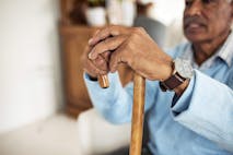 Photo: LaylaBird/MOYO STUDIO PTY LTD via Getty Images Close-up of an elderly man's hands holding a wooden cane. The man is wearing a blue sweater and a watch on his left hand.