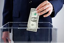Photo: Getty Images A male hand voting with money. Bribe - stock photo