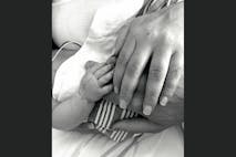 Black-and-white image of a stillborn baby's hand with her parents' hands.