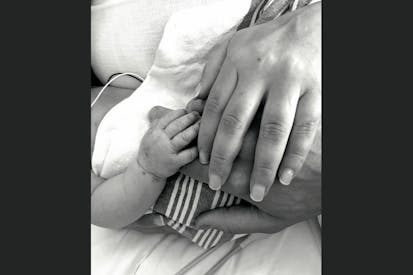 Black-and-white image of a stillborn baby's hand with her parents' hands.