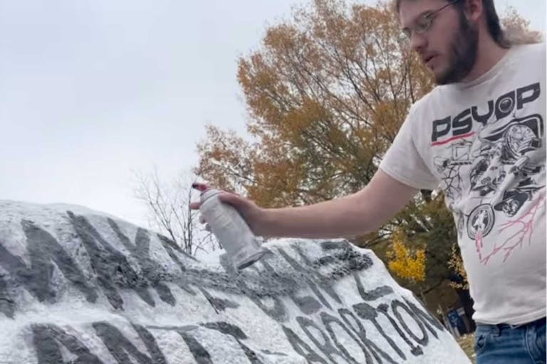 A man sprays paint over pro-life writing on The Spirit Rock at the University of Mary Washington