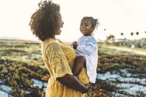 Pregnant mother holding young toddler girl on belly at beach