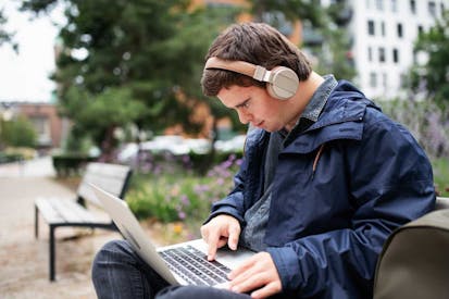 Man with down syndrome sitting on bench and working on laptop.
