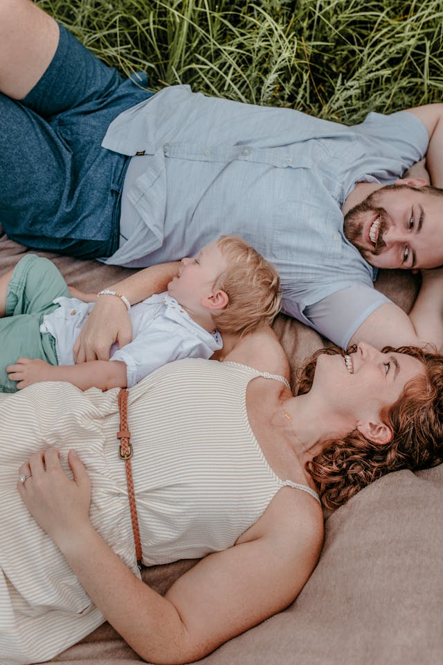 Photo: The Keller family before Jonah's diagnosis. Courtesy of the Keller family. Image shows husband, his wife, and their young son lying in the grass.