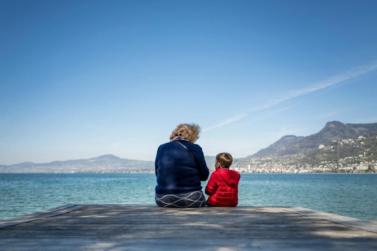 Photo: Fabrice Coffrini/AFP via Getty Images An elderly woman speaks with a young boy under a clear sky, on the edge of Lake Geneva in Villeneuve, western Switzerland, on April 8, 2025.