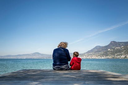 An elderly woman speaks with a young boy under a clear sky, on the edge of Lake Geneva in Villeneuve, western Switzerland, on April 8, 2025.