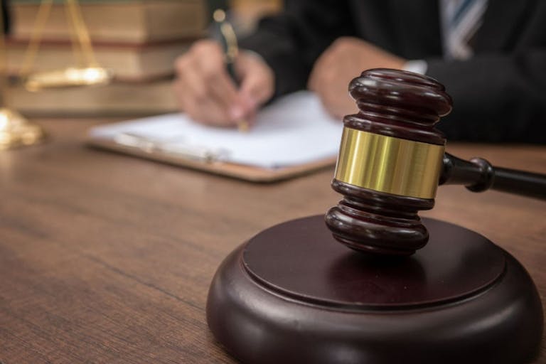 Photo: Boonchai Wedmakawand/Getty Images The image shows a gavel in the foreground with a judge signing paperwork in the background.